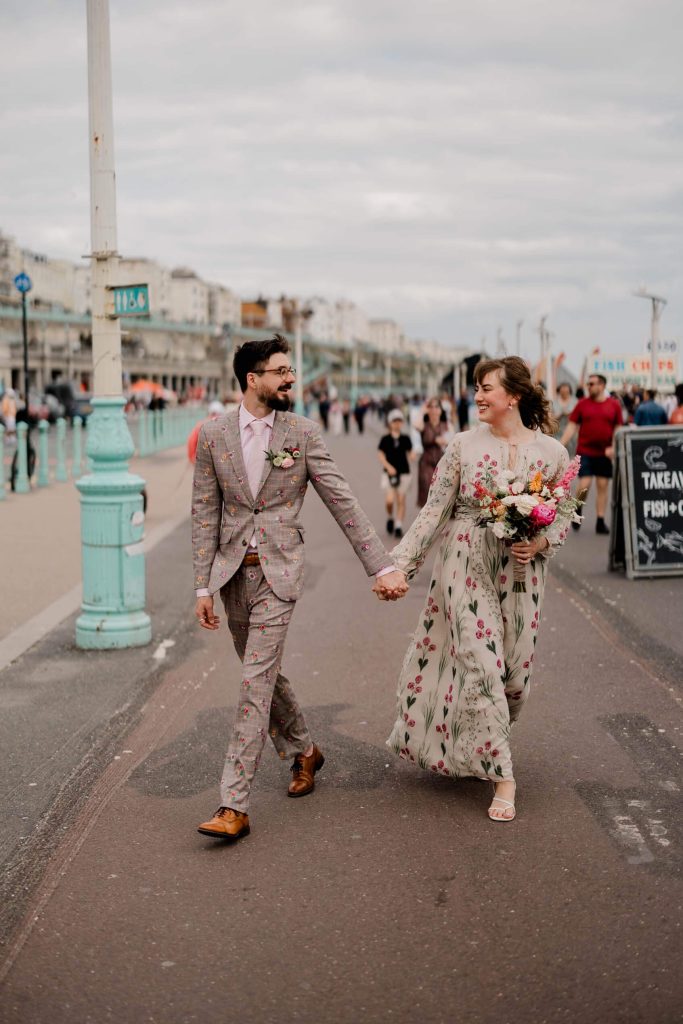 "Bride and groom smiling together on Brighton Pier, with a lively background of Brighton’s busy seafront"